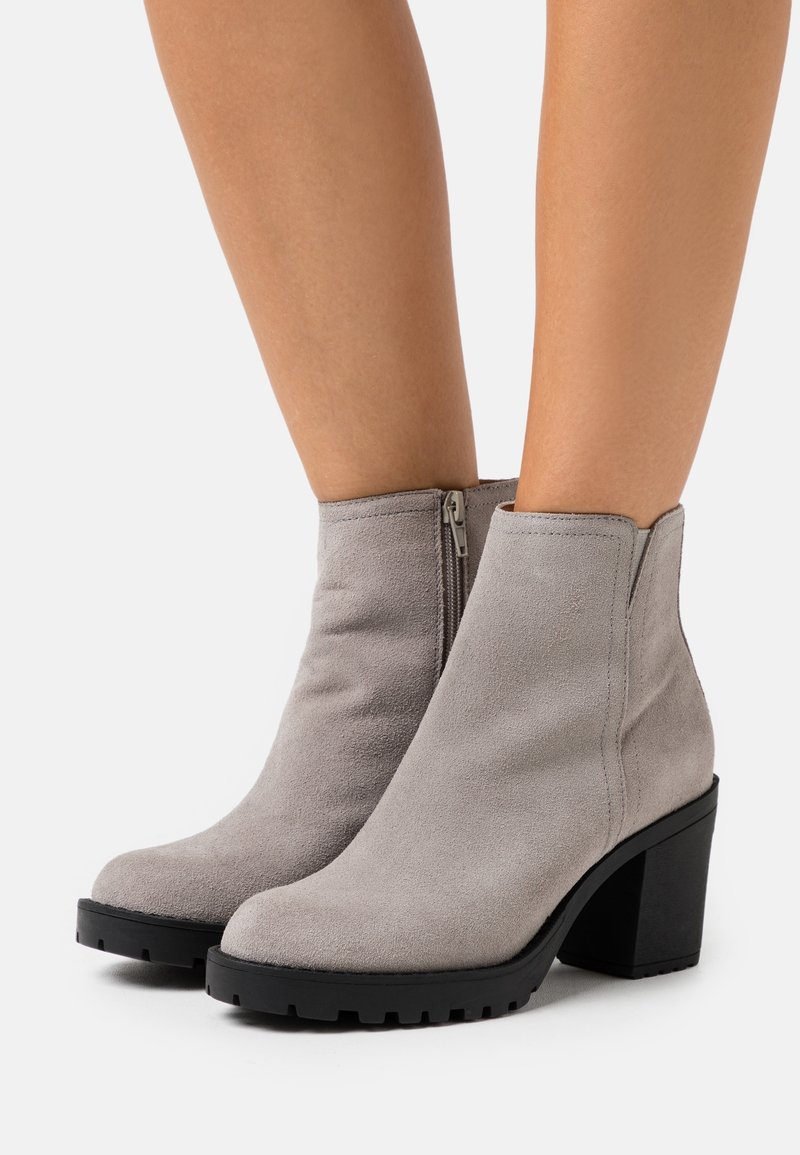 Botines de ante gris con una suela negra gruesa y una cremallera lateral. Punta redondeada y textura suave. Tacón bloque de altura media.