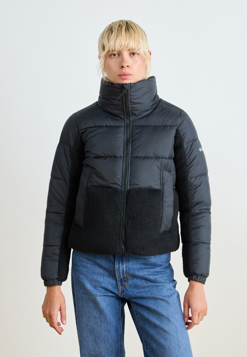 Svart dunjakke med høy krage, som har et mykt, fleece-lignende bunnpanel og elastiske mansjetter. Glidelås foran.