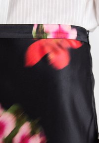 Sort med blomsterdesign i svart silke som har livlige rosa og grønne farger, glatt tekstur, og en slank utforming med en subtil glans.
