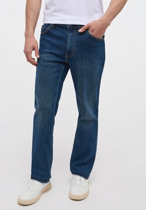 Jeans din denim albastru cu o croială dreaptă, prezentând o ușoară decolorare, cinci buzunare și cusături contrastante. Purtați cu adidași albi.