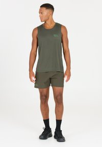 Olivgrön linne med en strukturerad mönster, kombinerat med matchande shorts. Svarta träningsskor och strumpor fulländar outfiten.