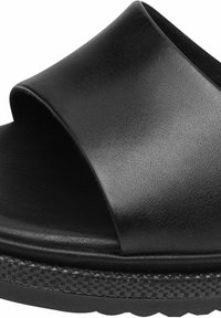 Svart läderslinga sandaler med en bred öppen ovansida, texturerad yta och en tjock vävd plattformssula. Slät och minimalistisk design.