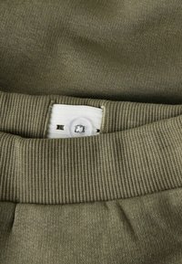 Olivengrønn sweatshirtstoff med ribbestrikkede mansjetter og en hvit etikett med knapphull. Myk tekstur med et strikkemønster.