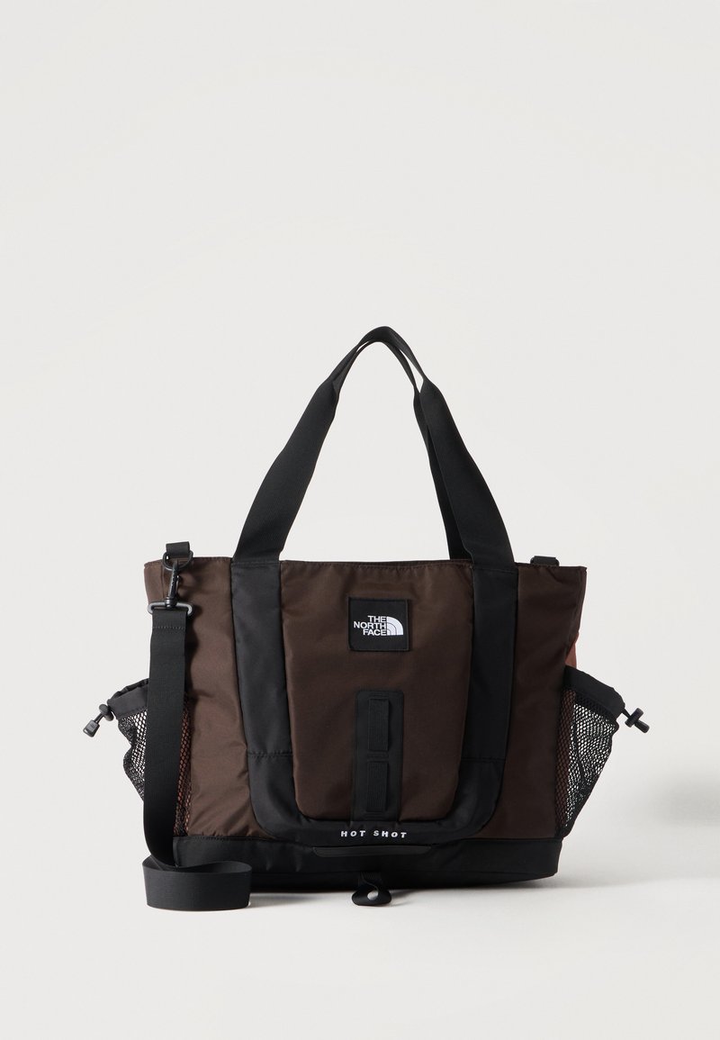 Καφέ και μαύρη τσάντα North Face με διπλές χειρολαβές, ρυθμιζόμενο λουράκι ώμου και πλεκτές πλαϊνές τσέπες σε απλό φόντο.