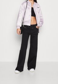 Ljust lila satin bomberjacka med elastiska ärmslut, svart crop top, högmidjade svarta jeans och vita sneakers. Inkluderar en liten svart väska.