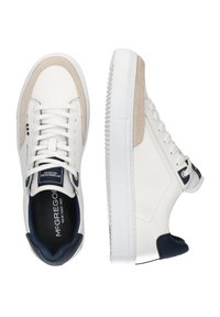 Sneakers hebben een bovenwerk van wit leer, beige suède accenten, een marineblauwe hak, een rubberen zool en ronde veters. Merken worden weergegeven op de tong.