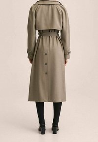 Abrigo largo tipo gabardina en verde oliva con cintura entallada, gran cuello y botones en la parte trasera. Hecho de tela suave con bolsillos laterales y mangas anchas.