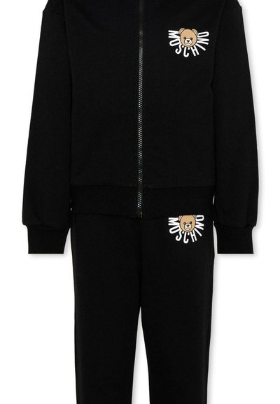 Tuta nera a due pezzi con giacca con zip e pantaloni, con logo orsetto e scritta "MOSCHINO" sul petto e sulla coscia.
