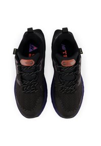 Zapatillas deportivas negras con un exterior texturizado, que presentan patrones de espiga, cordones reflectantes y acentos morados en la suela y la marca.