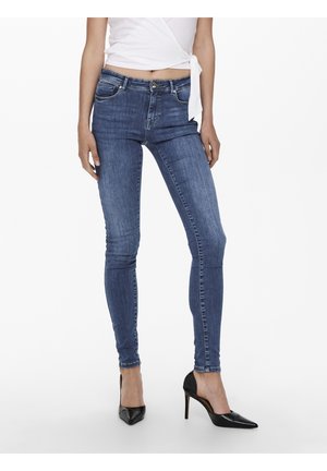 Jeans ajustados en denim azul medio, con cinco bolsillos, cremallera y botón, y una silueta entallada. Combinados con tacones negros de punta.