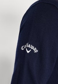 Námořnický modrý svetr s texturovaným povrchem, se bílým vyšitým logem "Callaway" a akcentem na rukávu. Měkký pletený materiál.