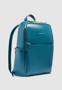 Turquoise leren rugzak met gouden ritsen, een voorvak en twee gewatteerde schouderbanden. Gladde textuur en rechthoekige vorm.