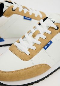 Zapatillas blancas y beige con un acabado texturizado, que presentan cordones blancos, una etiqueta azul con la inscripción "INSIDE" y una suela de goma negra.