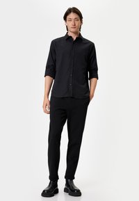 Zwarte overhemd met opgerolde mouwen, gecombineerd met zwarte slim-fit broek en zwarte enkellaarsjes, allemaal in effen kleuren, zonder patronen.