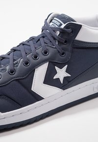 Námořnické plátěné tenisky s bílou hvězdou a akcenty. Mají textura povrchu, polstrovaný límec a kulaté tkaničky. Gumová podešev.