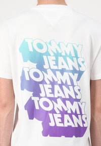 Hvid bomulds t-shirt med en gradient tekstprint i blå til lilla, der står "TOMMY JEANS" i fed skrift, i et gentaget design.