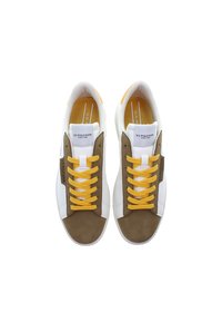 Hnědé a bílé tenisky s nubukovou špičkou, texturovanými bílými panely a žlutými tkaničkami. Branding na boku a měkké stélky.