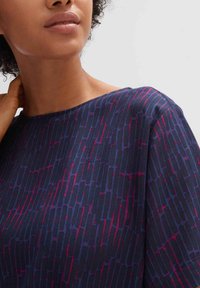Blusa blu navy con un motivo testurizzato di linee verticali rosa e viola. Collo ampio e maniche corte. Tessuto morbido.