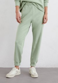 Muntgroene joggers gemaakt van zachte stof, met een elastische tailleband, taps toelopende boorden en zijzakken, gecombineerd met witte sneakers.