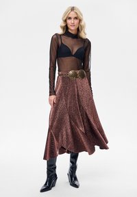 Czarny przezroczysty top z długim rękawem, pod spodem braletka. Błyszcząca brązowa spódnica midi o zwiewnym kształcie i ozdobnym złotym pasku. Czarne kozaki sięgające do kolan.