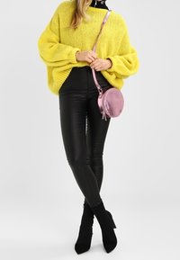 Suéter amarillo de punto grueso, leggings de cuero negro brillantes y un pequeño bolso cruzado rosa redondo. Botines negros de punta completan el look.