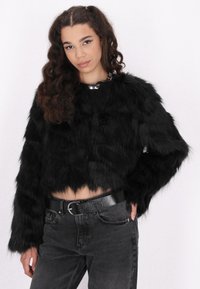 Zwarte faux fur gekorte jas met lange mouwen en een gestructureerde afwerking. Gecombineerd met donkerdenim jeans en een zwarte riem. Accented met een zilveren ketting.