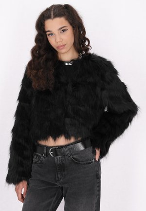 Zwarte faux fur gekorte jas met lange mouwen en een gestructureerde afwerking. Gecombineerd met donkerdenim jeans en een zwarte riem. Accented met een zilveren ketting.