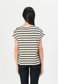 Stripet topp med marineblå og kremfargede horisontale striper, korte ermer med krage, en avslappet passform og en rund halslinning, kombinert med mørke jeans.