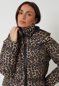 Vycpaná bunda s černobéžovým vzorem leopardího tisku, vysoký límec, zipový uzávěr a patentky na ramenech.