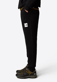 Czarne dresy z białą naszywką logo, o zwężanym kroju. W połączeniu z ciemnymi butami turystycznymi z żółtymi akcentami.