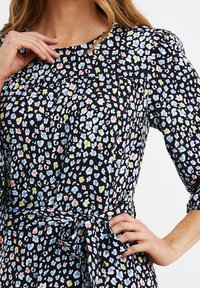 Vestido negro con un colorido estampado floral en tonos azules, rosas y verdes. Manga abullonada y detalle de cintura atada. Textura de tela suave.