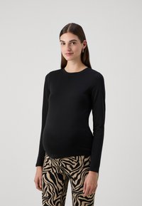 Juoda ilgomis rankovėmis palaidinė su apvaliu iškirpimu, derinama su smėlio ir juodais zebra rašto kelnėmis, turinčiomis tekstūruotą audinį.