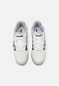 Witte en grijze sneakers met een geperforeerd leren bovenwerk, zwarte accenten en platte witte veters. Beschikt over een gewatteerde kraag en een logo op de tong.