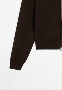 Maglione marrone a maglia con zip frontale, polsini e orlo a coste. Caratterizzato da una texture liscia e un design aderente.