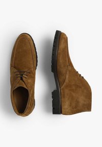 Brune ruskindssko med en glat overflade, der har en rund tå, snørebånd og en kraftig sort gummisål.