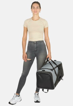 Schwarze und graue Sporttasche mit zwei Traggriffen, rechteckiger Form und strukturiertem Stoff, gehalten von einer Person in einem hellen Oberteil und Jeans.