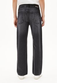 Donkergrijze wijde jeans met een hoge taille, voorzien van twee achterzakken en zichtbare naden, gestyled met een casual wit shirt en sneakers.