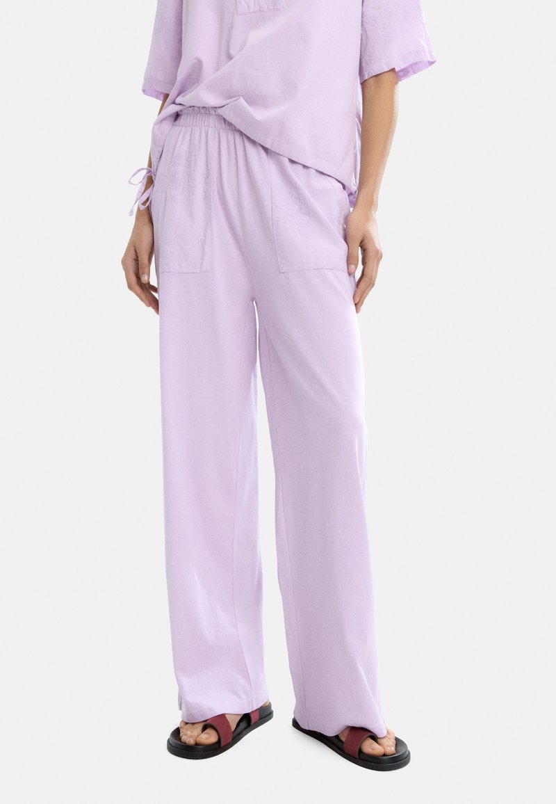Jasnofioletowe, luźne spodnie z elastycznym pasem, bocznymi kieszeniami i miękką fakturą, w połączeniu z czarnymi i bordowymi sandałami.