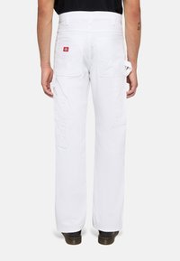 Pantalones cargo blancos con corte recto, múltiples bolsillos y un parche de logo rojo, fabricados con tela duradera. Con trabillas visibles y detalles en los laterales.