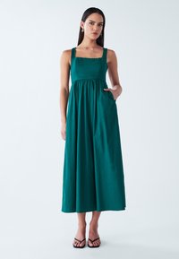 Tumesinine maksikleit ruudukujulise dekolteega, laiad rihmad ja kitsas kehaosa. Omaduseks voolav seelik ja küljetaskud. Sile tekstuur.