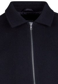 Svart zip-up jacka med krage, tillverkad av ett texturerat tyg. Har en metallblixtlås och en minimalistisk design.