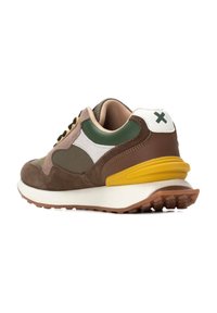 Zapatilla marrón y verde con parte superior de ante y malla, acentos blancos, tapa de talón amarilla, cordones negros y suela de goma texturizada.