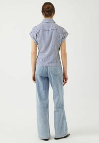Camicia a righe blu e bianche con maniche corte, abbinata a jeans a gamba larga di un blu chiaro. L'outfit presenta un design semplice e casual.