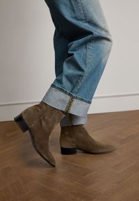 Stivaletti in suede marrone con punta appuntita e tacco nero basso, abbinati a jeans in denim azzurro chiaro con risvolto e cuciture in contrasto.