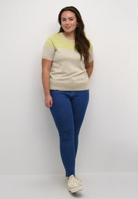 Beige short-sleeve sweater with green horizontal stripes, paired with blue skinny jeans and white sneakers. Simple design, soft texture.