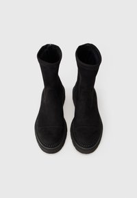 Bottines en daim noir avec une texture lisse, des poignets élastiques, des coutures renforcées et des semelles en caoutchouc. Design simple, sans quincaillerie visible.