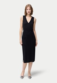 Svart ärmlös klänning med V-ringning, midjebälte och två framfickor, tillverkad av ett slätt tyg med sidospjäll för rörelsefrihet.