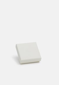 Bela kvadratna škatla z teksturirano površino, ki ima na vrhu subtilen vtisnjen logo. Zaobljeni koti in minimalistična zasnova.