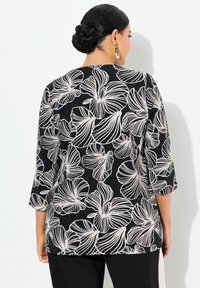 Schwarze Bluse mit weißen floralem Linienstil, Dreiviertelärmeln und lässiger Passform. Das Material wirkt glatt und hat eine leichte Textur.