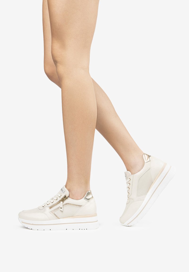 Beige sneakers with leather and mesh panels, featuring a zipper, metallic accents, and a white sole. Eased fit for comfort.
